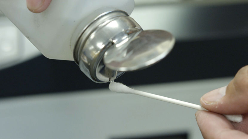 Apply rubbing alcohol to a cotton swab. Pouring rubbing alcohol onto a cotton swab.