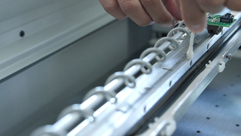 Run the cotton swab along the back of the encoder strip. Cleaning the back of the linear encoder strip.
