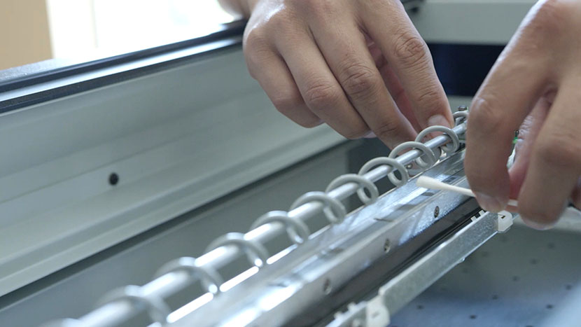 Run the cotton swab along the top of the encoder strip. Cleaning the top of the linear encoder strip.