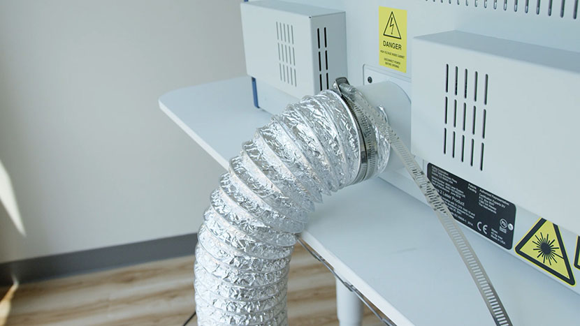 Hook up the exhaust hose to the machine. An air ducting tube being attached to the exhaust port on the Epilog Laser Zing.