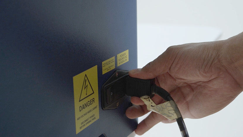 Turn off the laser and remove the power cord from the machine. Unplugging the power cord from the Epilog Laser Zing.