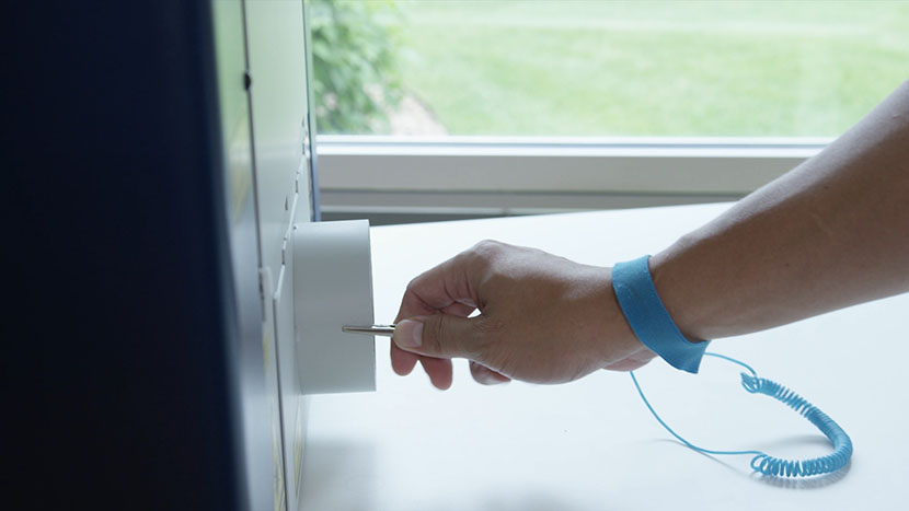 Put on the anti-static strap and clip it to the machine. Clipping a wrist-mounted static strap to the exhaust port of the machine.
