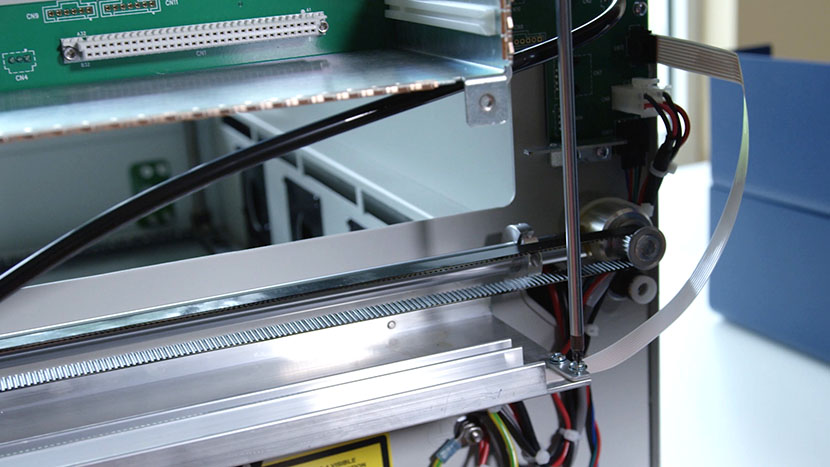 Remove the flex cable clamp. Unscrewing the flex cable clamp at the back right of the machine.