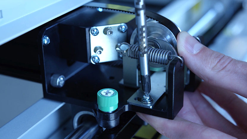 While pushing the idler toward the machine, tighten the Phillips screws. Tightening the Phillips screws while pushing the idler bracket against the machine.