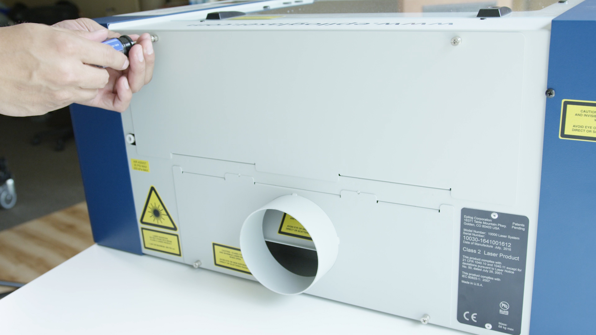 Remove the rear panel by loosening the two screws on the back of the machine. Unscrewing the top left screw of the Zing's rear panel.