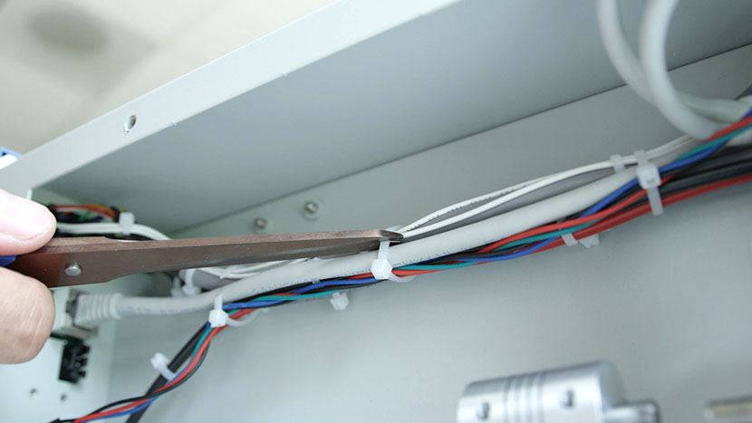 Cut all three white cable ties securing the wires. Scissors preparing to cut the middle zip tie around the rear compartment wires.